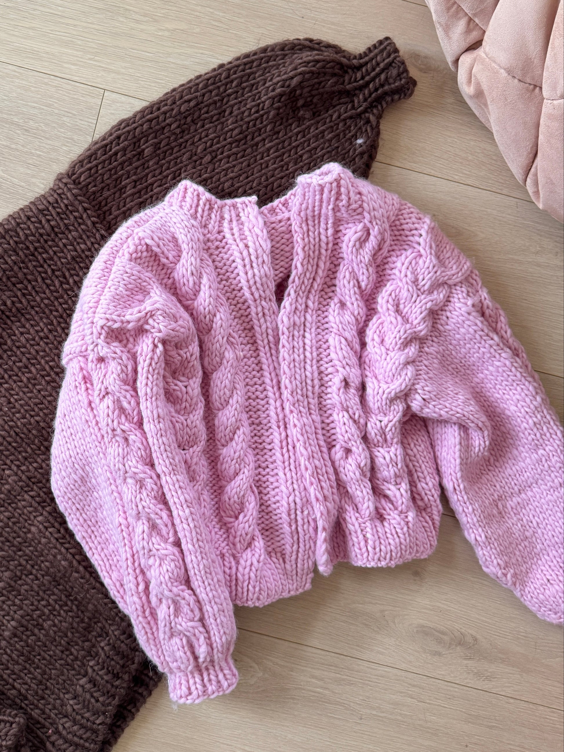 Pink and brown knitted sweaters on a light wooden floor